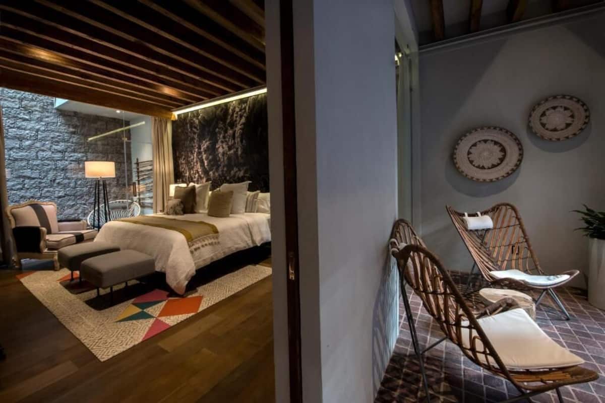 Un dormitorio con cama, mesitas de noche, una silla y vistas al exterior.