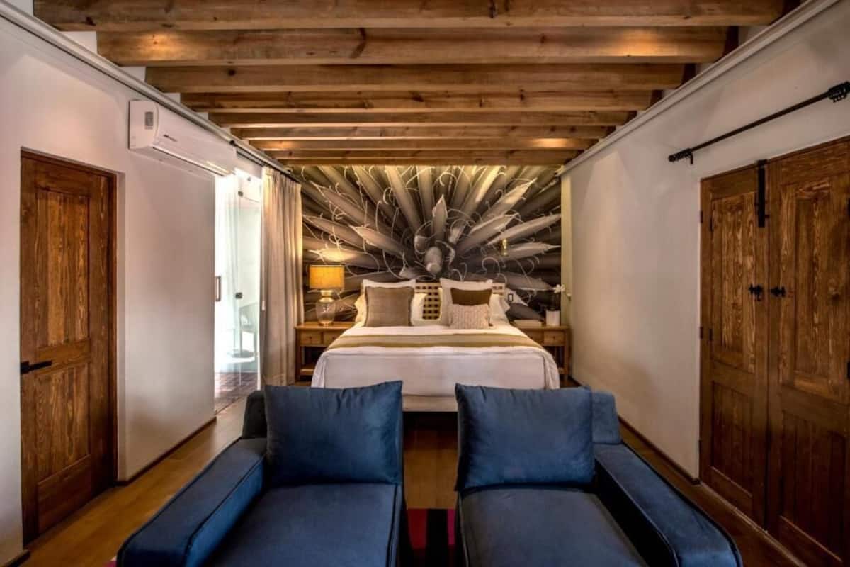 Un dormitorio con una cama grande, vigas de madera en el techo y dos sofás azules.