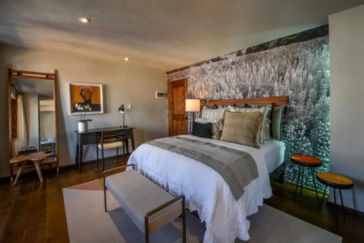 Un dormitorio con una cama grande, un escritorio, una silla, un banco y un mural de un bosque en la pared.