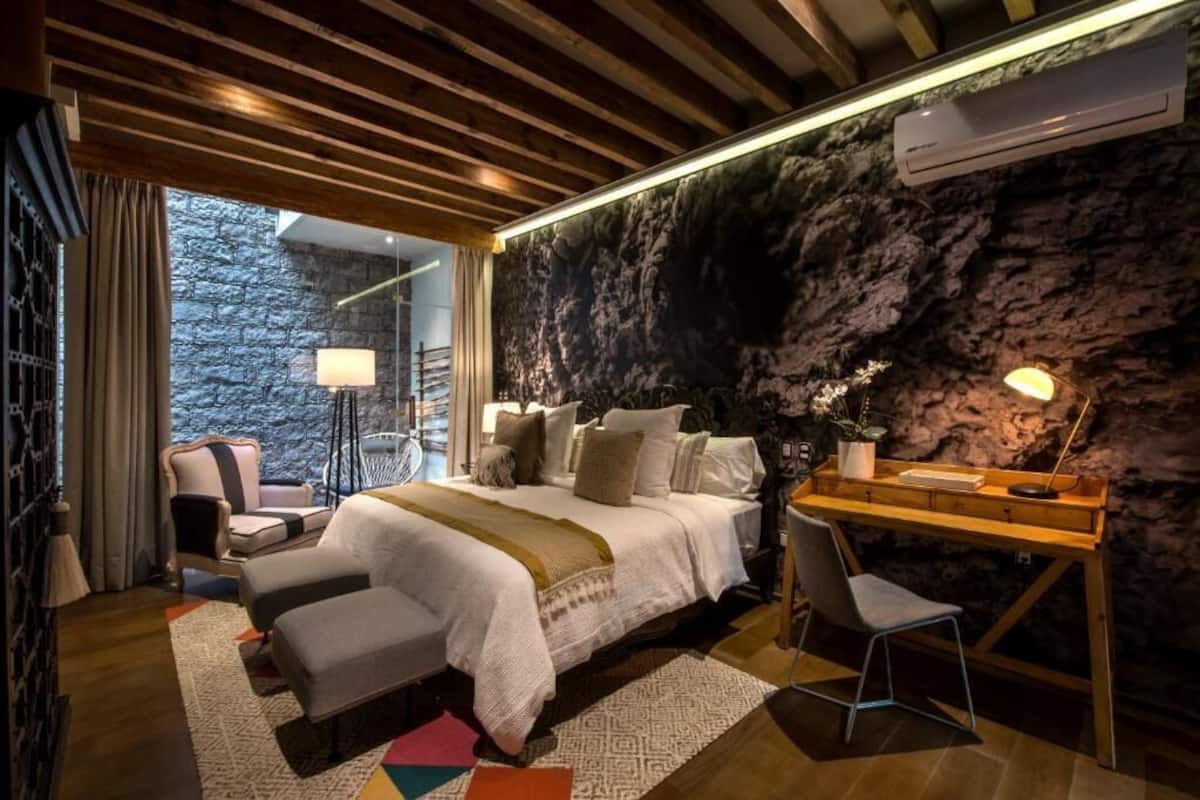 Un dormitorio con cama, escritorio, silla, lámpara y vistas al exterior.