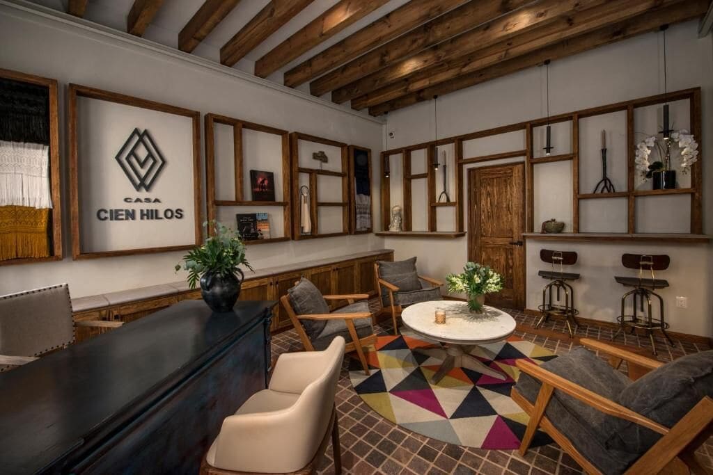 A modern interior with a wooden ceiling, a reception desk, seating area, and a decorative wall with a logo.