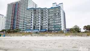 A high-rise hotel with multiple balconies, located adjacent to a sandy beach. - ⛱ DIRECT OCEANFRONT⛱ PENTHOUSE VIEW! ALL NEW LARGE BALCONY! ALL NEW RENOVATION! (Myrtle Beach)