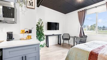 Quarto de hotel moderno com cozinha compacta, televisão de tela plana, cama com colcha, escrivaninha e uma cadeira.