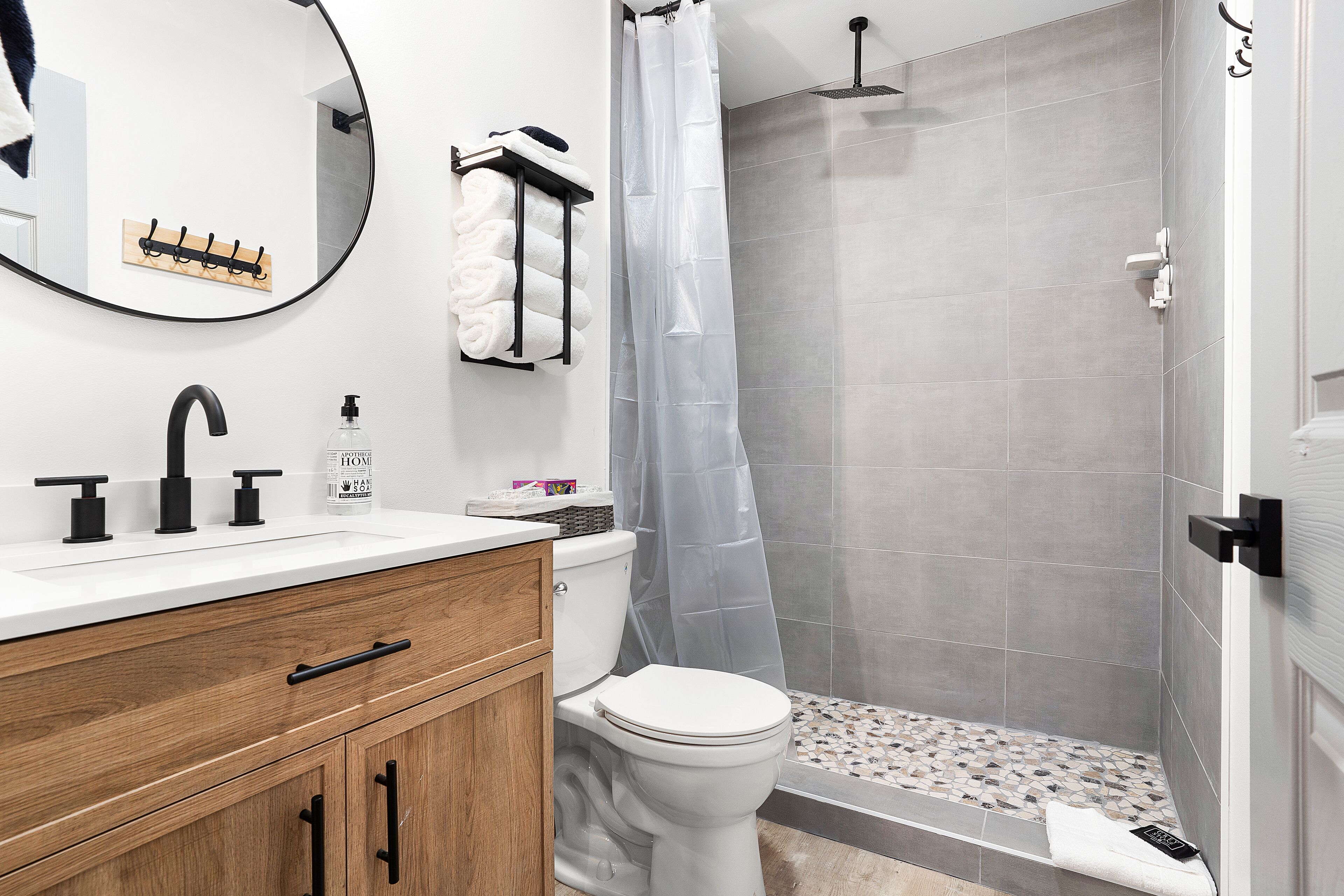 A modern bathroom with a white sink, black faucet, wooden cabinet, and a shower area with grey tiles.