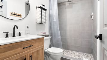 A modern bathroom with a white sink, black faucet, wooden cabinet, and a shower area with grey tiles.