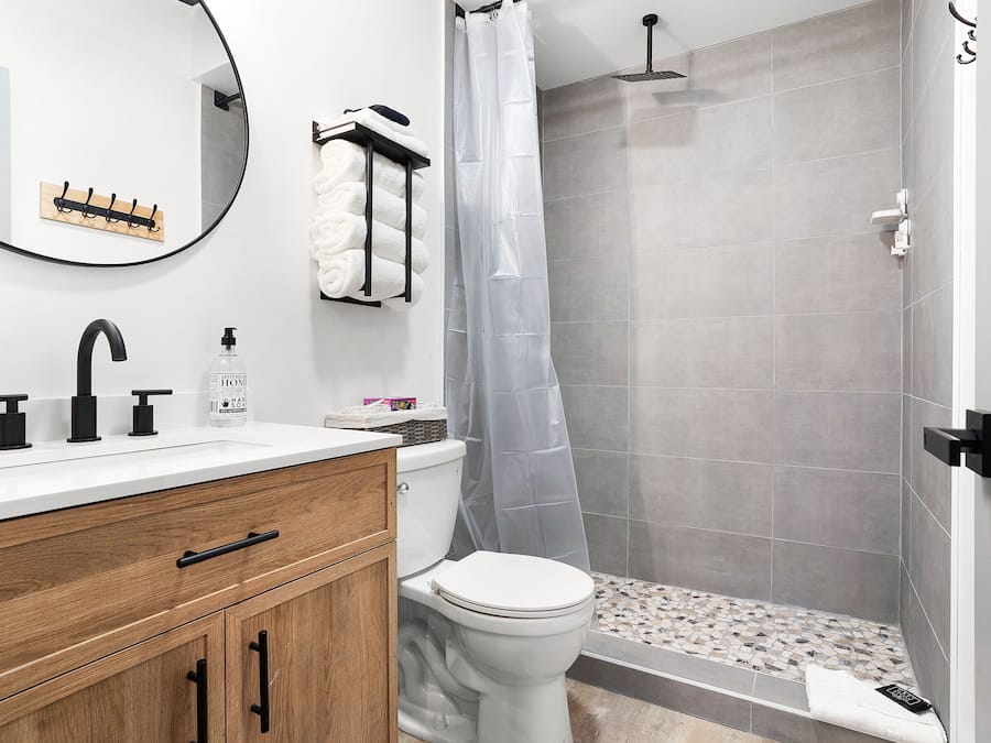 A modern bathroom with a white sink, black faucet, wooden cabinet, and a shower area with grey tiles.