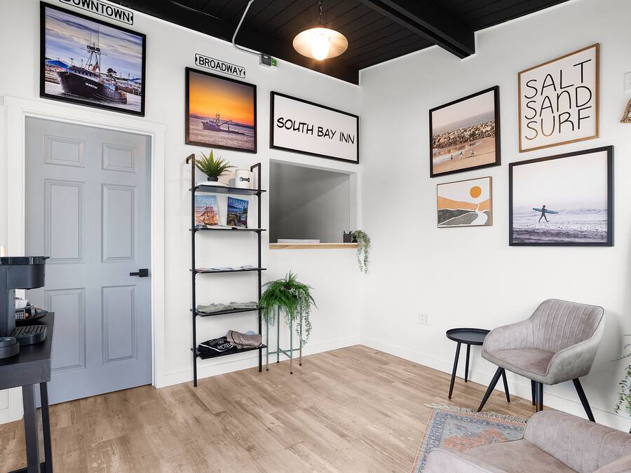 A modern room with a wooden floor, a grey armchair, a desk with a computer, and a bookshelf.