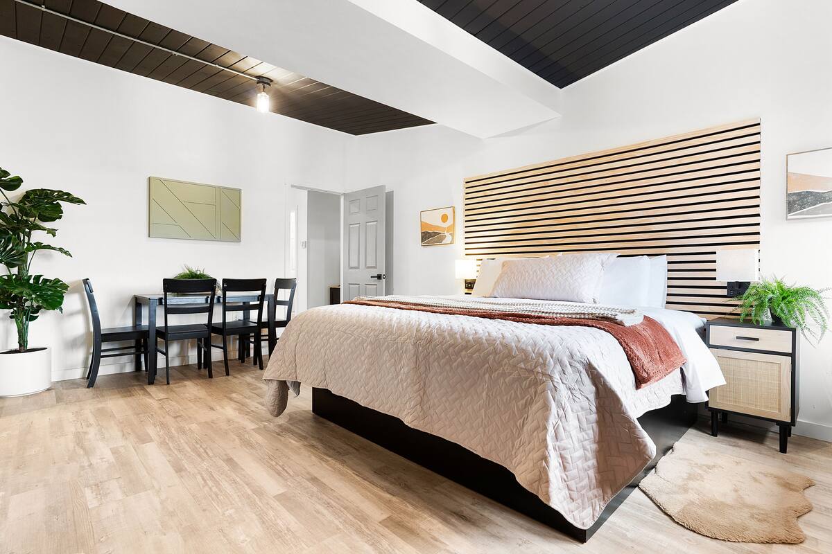 A modern bedroom with a bed, bedside table, and a dining area with chairs and a table.
