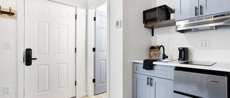 A modern kitchen with white cabinetry, a built-in microwave, and a stainless steel dishwasher.