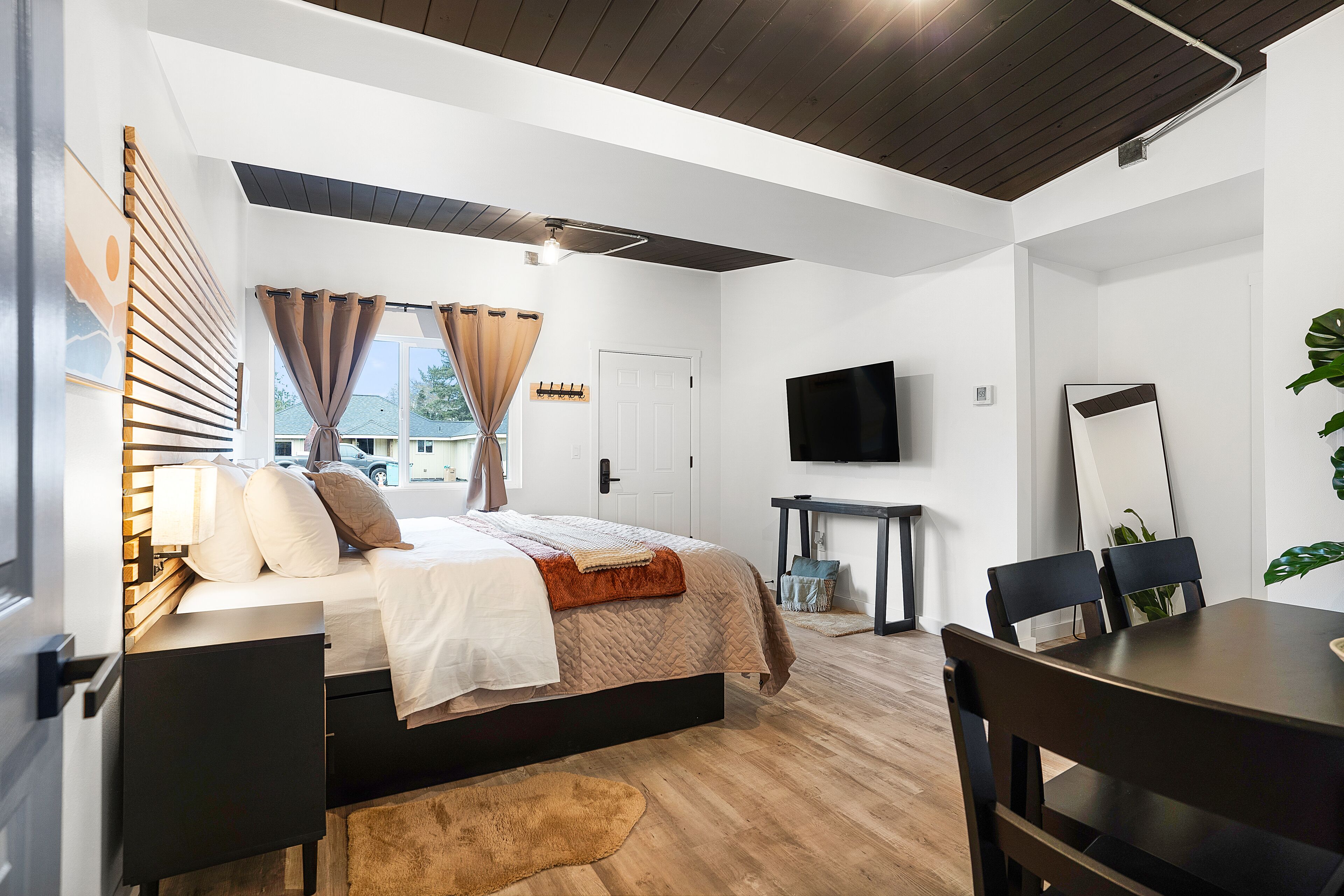 A modern bedroom with a bed, bedside tables, a TV, and a dining area.