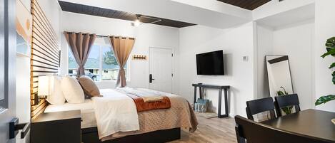 A modern bedroom with a bed, bedside tables, a TV, and a dining area.