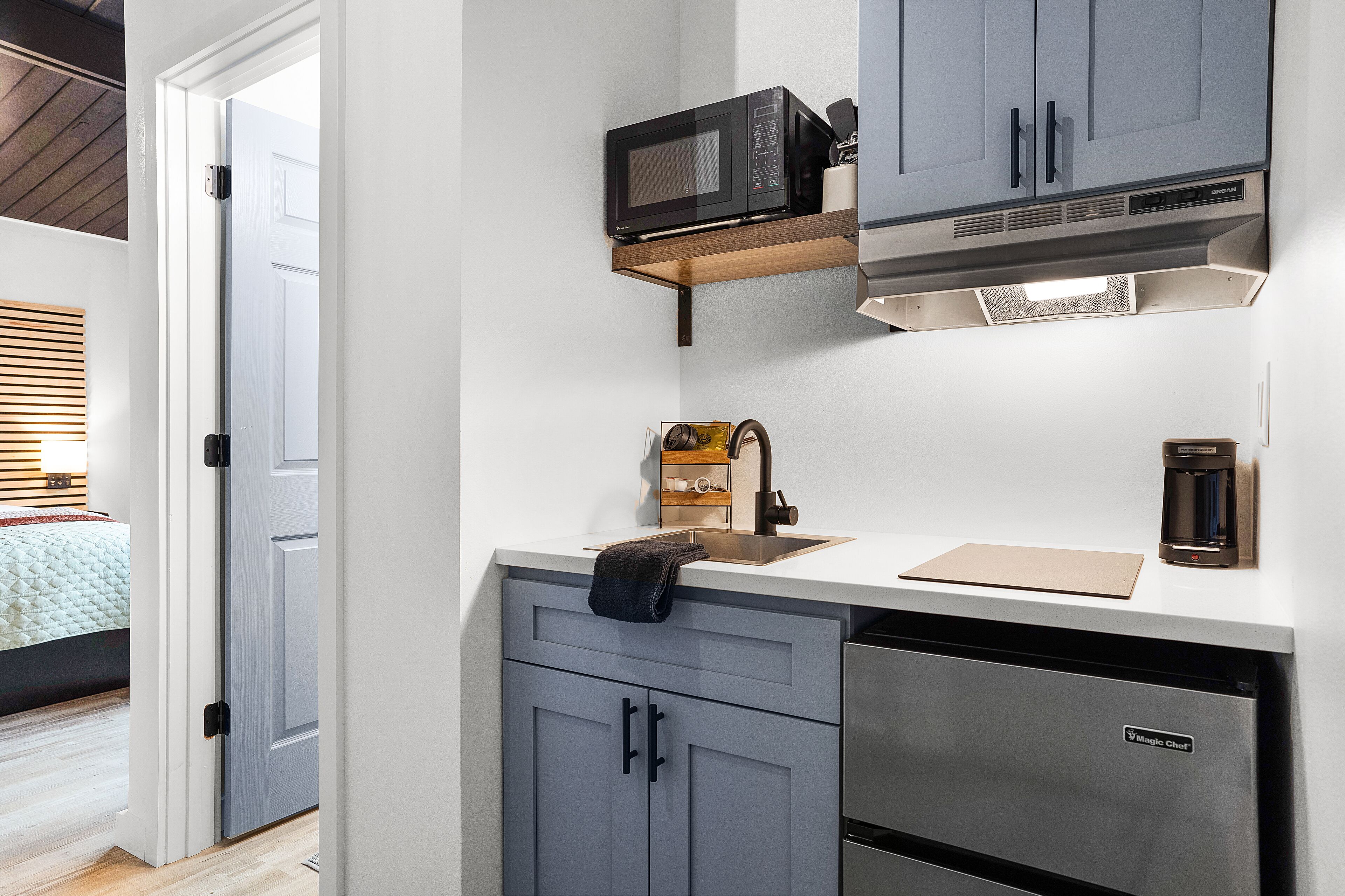 Uma cozinha compacta com armários cinzentos, micro-ondas, máquina de café e lava-louças.