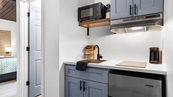 Uma cozinha compacta com armários cinzentos, micro-ondas, máquina de café e lava-louças.