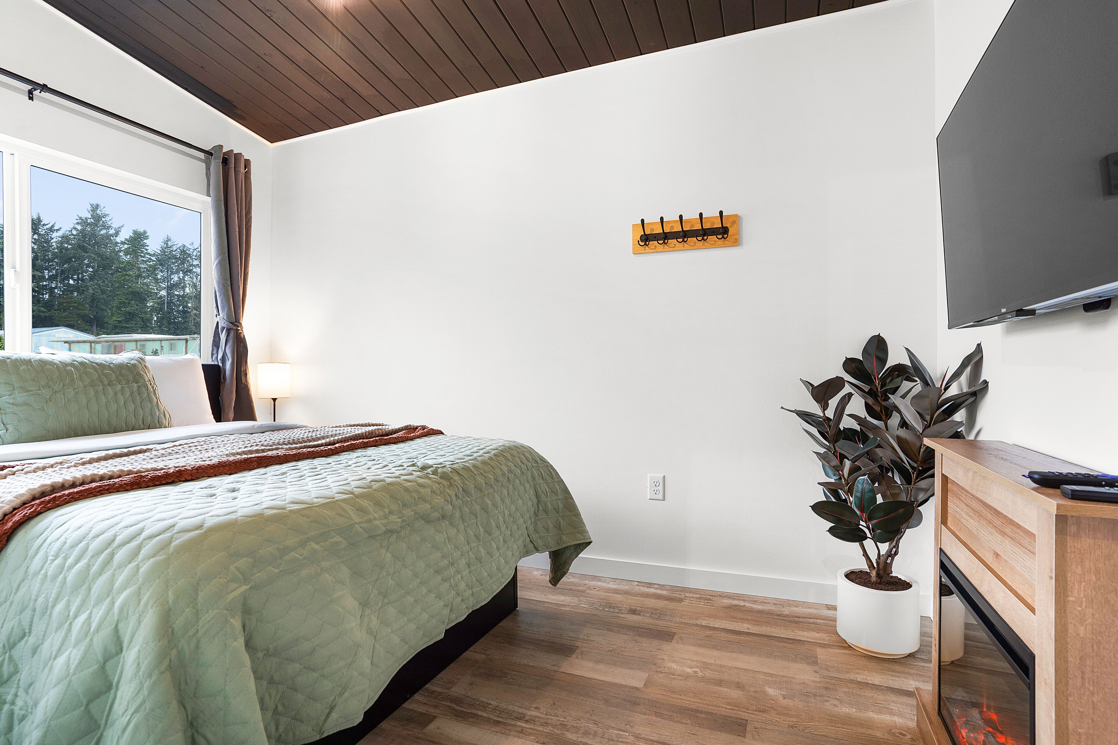 A bedroom with a bed, a bedside table, a potted plant, and a TV mounted on the wall.