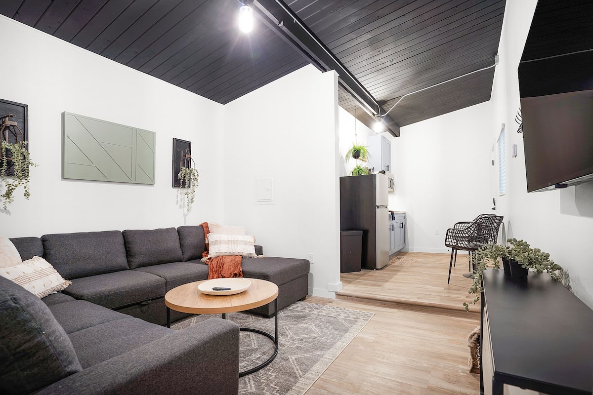 A modern living room with a sectional sofa, a round coffee table, and a TV mounted on the wall.