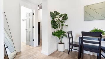 A modern interior with a wooden floor, a potted monstera plant, a dining table with chairs, and a large mirror.