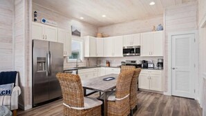 A modern kitchen with white cabinets, stainless steel appliances, and a dining area with wicker chairs. - That Sunset! Pool on the waters edge  (Rockport)