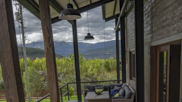 Un espacio de estar techado al aire libre con muebles de mimbre y vistas a montañas.