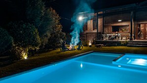 Una piscina con una fuente de agua azul cristalina, rodeada de césped cuidado y árboles.