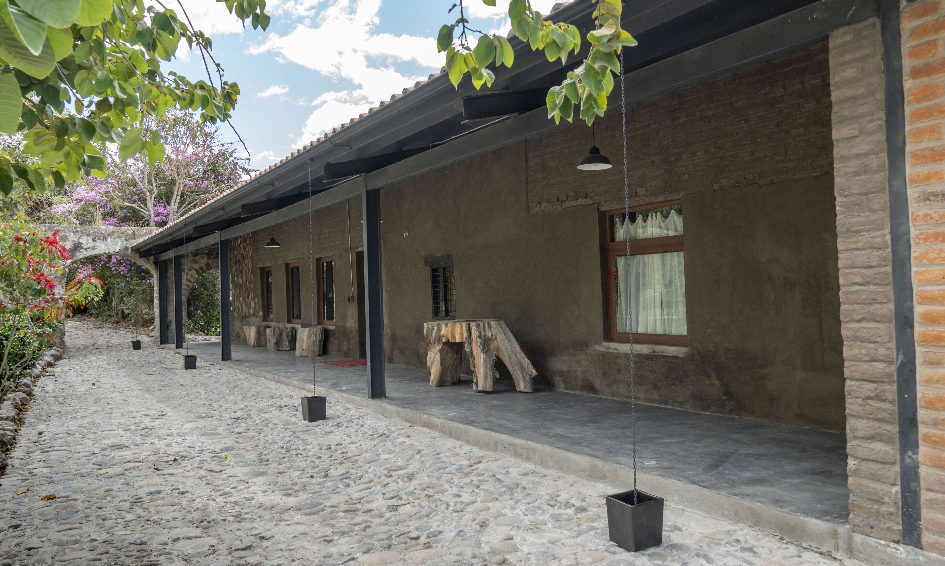 Un edificio rustico con facciata in pietra, diverse finestre e una zona esterna coperta con tavolo e sedie.