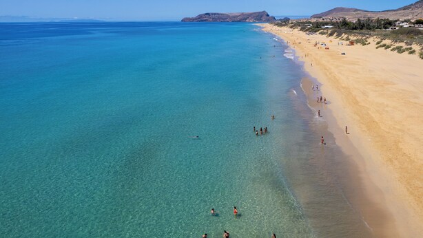 A beach with clear turquoise waters, sandy shore, and distant mountains.