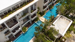 A multi-story hotel with a central swimming pool surrounded by lush greenery and balconies with plants. - NHOA 207B Lux 1BR Condo Pool View in Aldea Zama (Tulum)