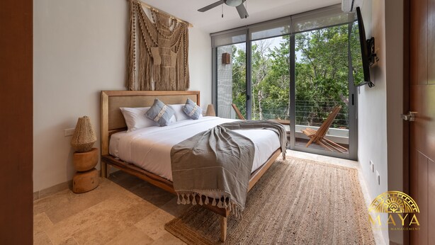A bedroom with a bed, a ceiling fan, a large window, and a view of trees. - NHOA 207B Lux 1BR Condo Pool View in Aldea Zama (Tulum)