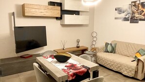 A modern living room with a dining area, a flat-screen TV, a pendant light, and a beige sofa. - A stone's throw from San Pietro and Villa Pamphili (Roma)