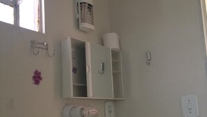 Un baño con espejo, secador de pelo, toallero, dispensador de papel higiénico e interruptor de luz.