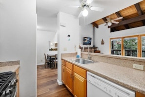 A kitchen with wooden cabinets, a granite countertop, a dishwasher, and a ceiling fan.