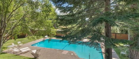 A backyard with a swimming pool, surrounded by trees and a patio area with chairs.
