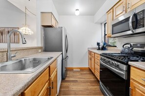 A compact kitchen with a stainless steel sink, wooden cabinets, a refrigerator, a microwave, and a stove.