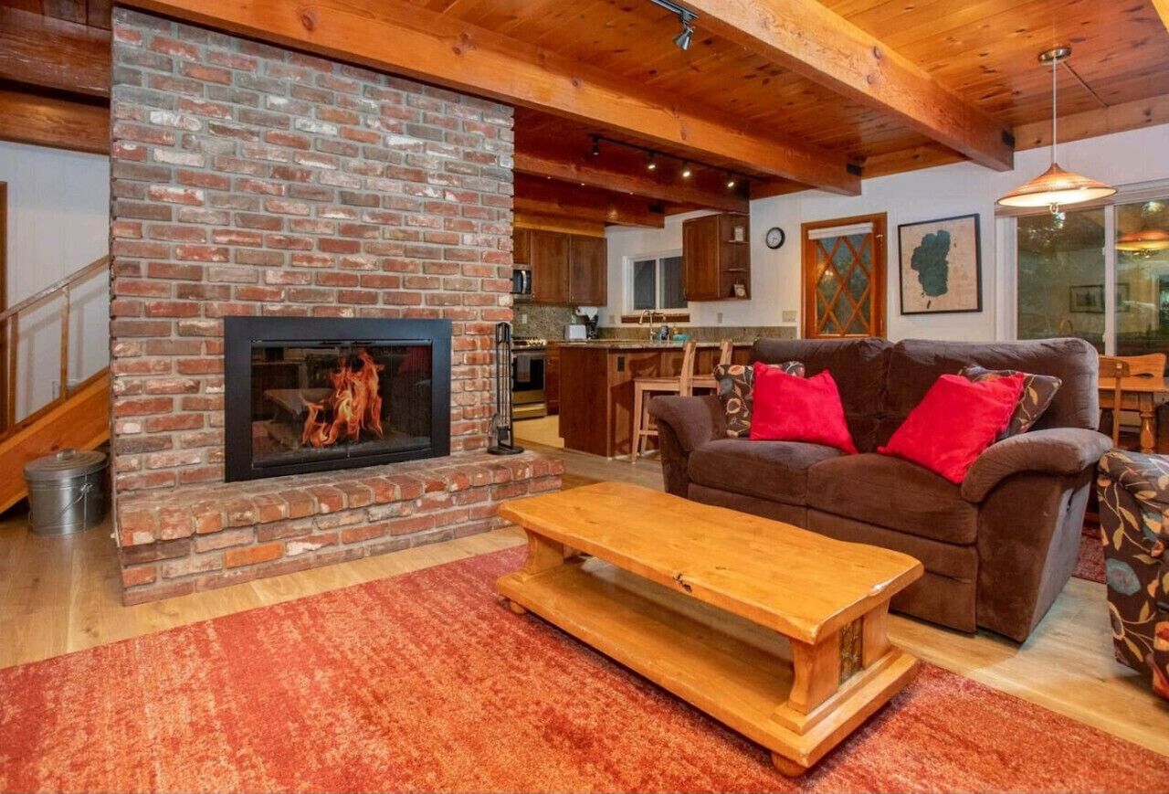 A cozy living room with a brick fireplace, a brown sofa with red cushions, and a wooden coffee table.