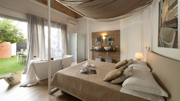 A bedroom with a large bed, a bathroom with a bathtub, and a view of a garden. - Villa Loria - Luxurious Villa with private pool located in the city centre (San Vito Lo Capo)