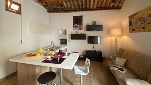 A modern kitchen with a white countertop, a dining area with a white chair, a sofa, and a TV on the wall. - Villa Loria - Luxurious Villa with private pool located in the city centre (San Vito Lo Capo)