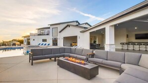 Uma área externa moderna com piscina, lareira e um amplo sofá modular cinza.