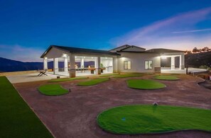 A modern house with a spacious patio area featuring green artificial grass and a well-lit interior.