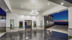 Amplo espaço interno com piso refletivo, um grande candelabro e vista para um pôr do sol pela janela.