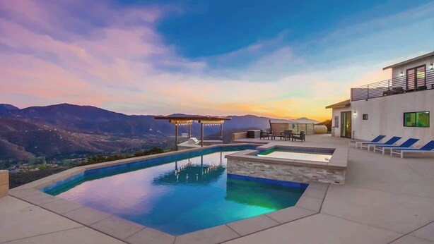 Uma área de piscina moderna ao ar livre com vista para montanhas, um espaço coberto para relaxar e um edifício com varanda.