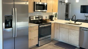 A modern kitchen with stainless steel appliances, wooden cabinets, and a central island. - Stay, play, relax- Sleeps 4, close to downtown with rooftop hot tubs! (Traverse City)