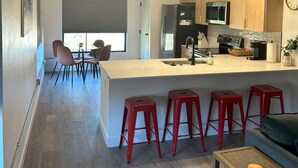 A modern kitchen with a central island, red bar stools, and pendant lighting. - Stay, play, relax- Sleeps 4, close to downtown with rooftop hot tubs! (Traverse City)