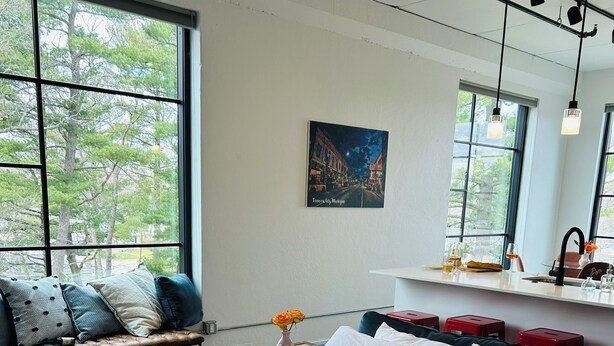 A modern bedroom with a large bed, a bench with pillows, a small table with a vase, and a painting on the wall. - Stay, play, relax- Sleeps 4, close to downtown with rooftop hot tubs! (Traverse City)