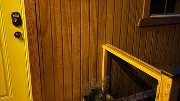 Une porte en bois ornée d’une guirlande rouge, un pot de fleurs contenant une plante étiquetée « gui », et un petit escalier en bois muni d’une rampe.
