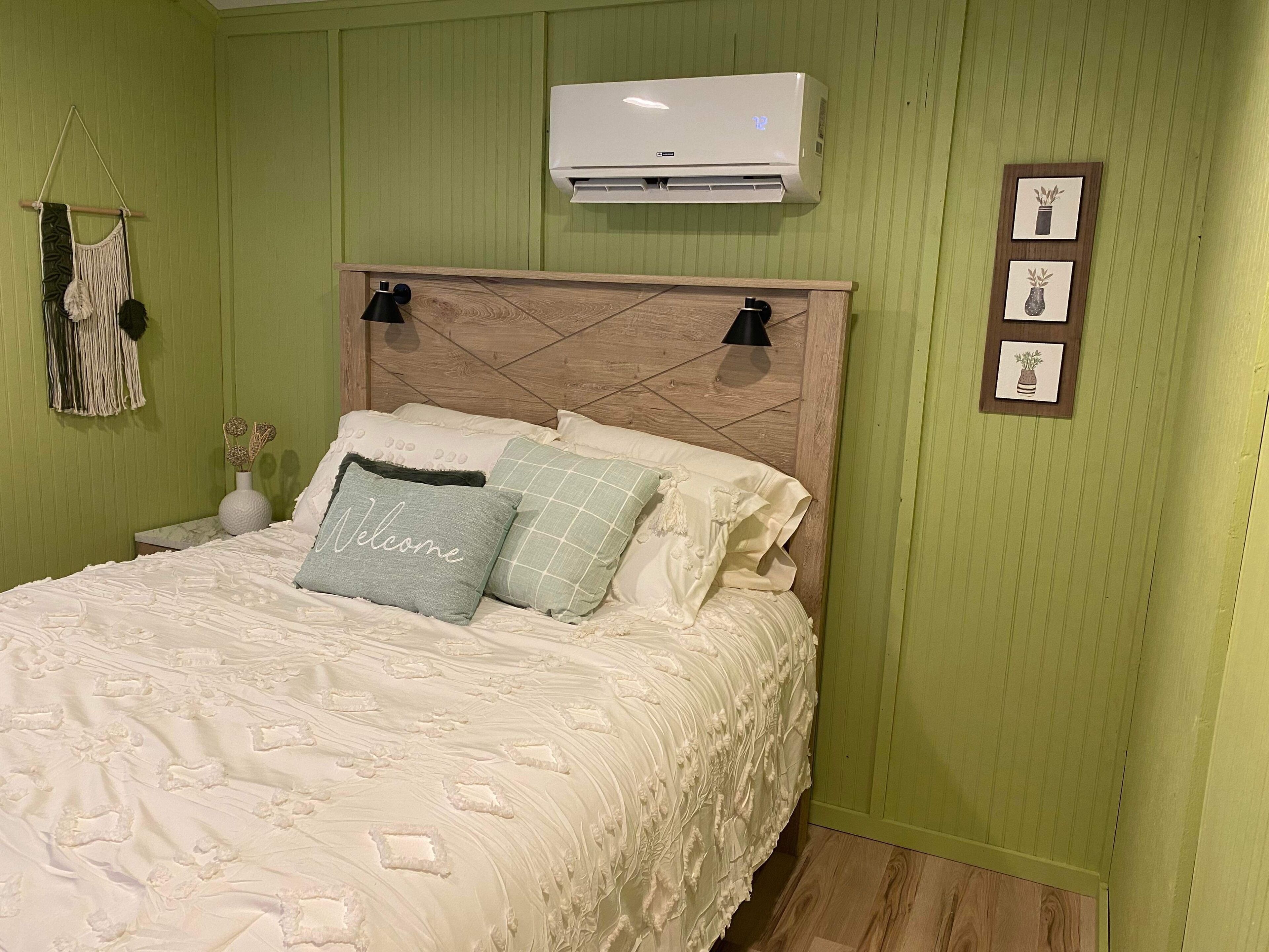 Un dormitorio con cama, aire acondicionado de pared y un tapiz de macramé.