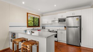 A modern kitchen with white cabinets, a stainless steel refrigerator, a microwave, and a large island with stools.