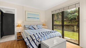 A bedroom with a bed, two bedside lamps, a framed picture, and a view of a garden through a sliding door.