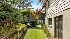 A residential property with a paved driveway, a wooden raised garden bed, and a variety of plants and shrubs.