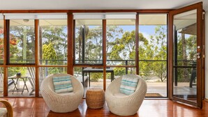 A spacious room with large glass doors leading to an outdoor area, featuring two wicker chairs with striped cushions and a woven basket on the floor.
