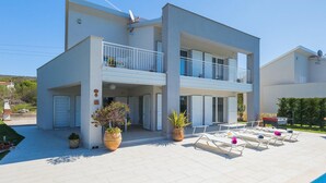 Un bâtiment moderne à deux étages, doté d’un toit plat, d’un balcon à l ’étage supérieur et d’un espace extérieur aménagé avec des fauteuils confortables.