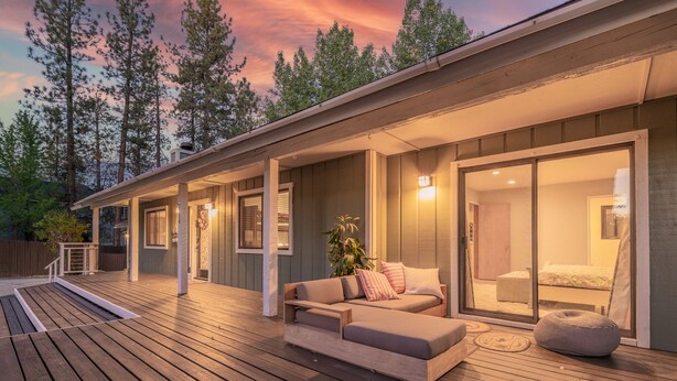 A modern house with a wooden deck, a sofa, and a large sliding glass door leading to a bedroom.